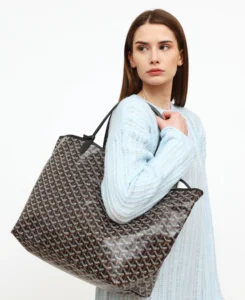Woman carrying a large Goyard bag Louis tote bag in brown chevron pattern, paired with a soft blue knitted dress, looking sideways.