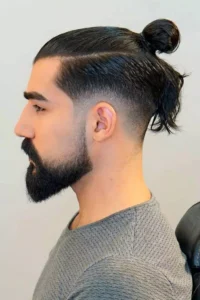 Man with a sleek undercut and long hairstyle tied in a top knot, showcasing a trendy men's long hairstyle.